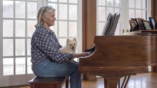 Жінка грає на фортепіано з собакою на ногах